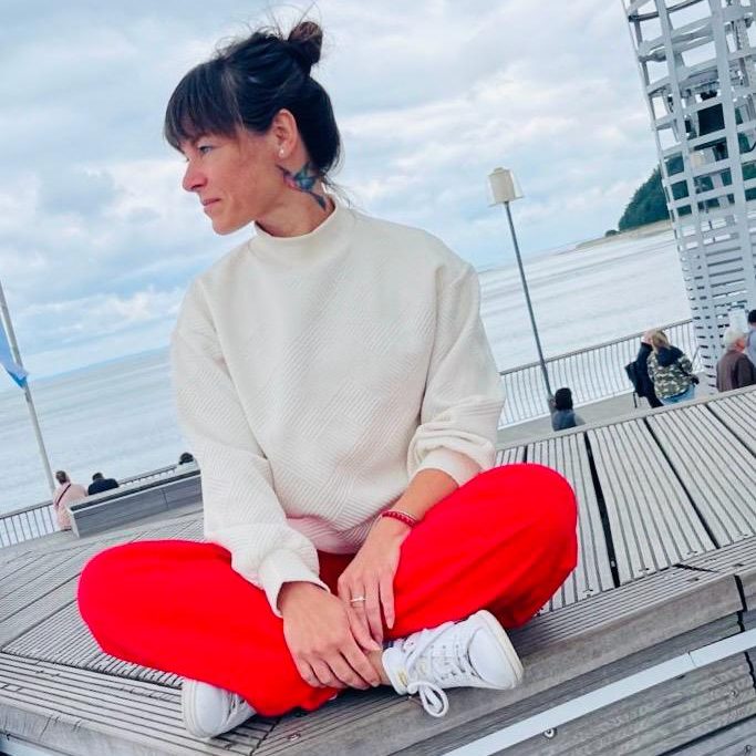 ostsee1 Inhaberin Kerstin König sitzt im Schneidersitz auf einem Holzpodest am Ostseestrand.